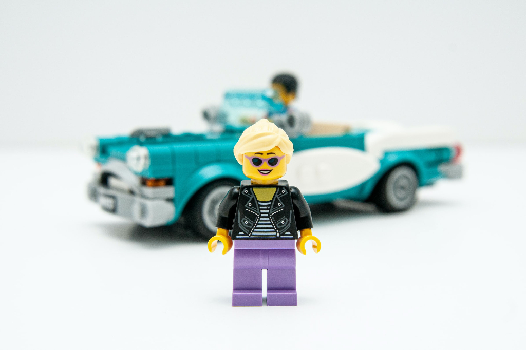 A happy Lego person with a Lego car in the background
