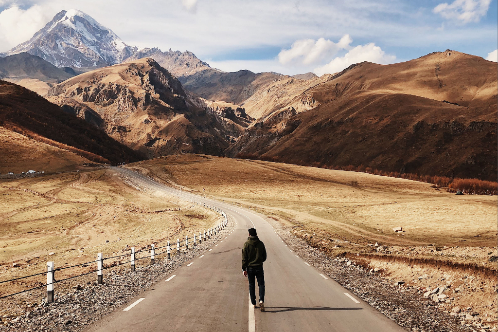 A lone man walking on a narrow paved country road